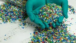 Two gloved hands hold small pieces of colourful plastic Two gloved hands hold small pieces of colourful plastic